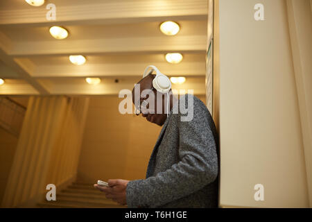 Seitenansicht Portrait von trendigen afrikanischer Mann Kopfhörer tragen und Sie ihr Smartphone in Designer Büro, Kopie Raum Stockfoto