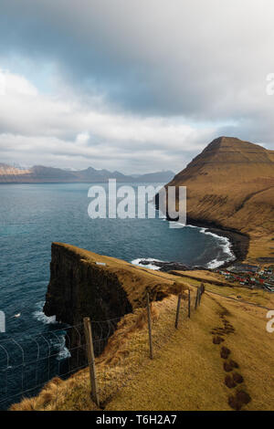 Das kleine Dorf Gjógv und die umliegenden Berge und das Meer, wie man es von einem steilen Felsen gesehen mit einem malerischen Wanderweg (Färöer, Dänemark, Europa) Stockfoto