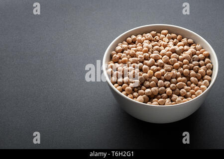 Trockene Kichererbsen in Weiß Schüssel auf dunklem Hintergrund isoliert Stockfoto