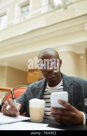 Porträt des zeitgenössischen afroamerikanischen Menschen studieren sitzen an einem Tisch in Cafe und Sie ihr Smartphone, kopieren Raum Stockfoto