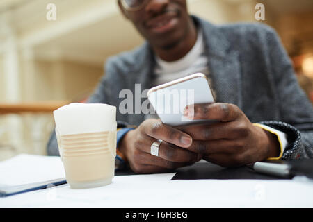 Den mittleren Abschnitt Porträt des zeitgenössischen afroamerikanischen Menschen studieren sitzen an einem Tisch in Cafe und Sie ihr Smartphone, kopieren Raum Stockfoto