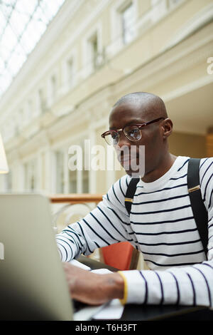 Portrait Zeitgenössischer Afrikanischer Student trägt eine Brille mit Laptop während des Studiums in Bibliothek, Raum kopieren Stockfoto