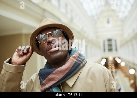 Kopf und Schultern Porträt des modernen afrikanischen Mann mit Hut und Trenchcoat, während in einem wunderschönen Gebäude im freien Raum darstellen, kopieren Stockfoto