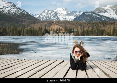 Junge Mädchen liegt auf hölzernen Terrasse von gefrorenen Bergen See Strbske Pleso - Frühling in der Hohen Tatra in der Slowakei. Stockfoto