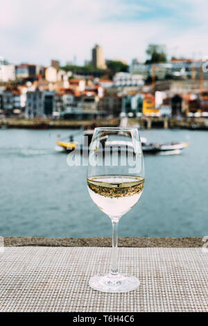 Selektiver Fokus auf Weißweinglas mit Blick auf den Vila Nova de Gaia Damm bei Cais da Ribeira am Fluss Douro in Porto, Portugal Stockfoto