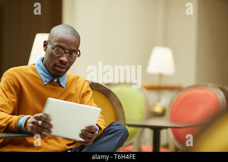 Porträt des zeitgenössischen afrikanischen Mann mit digitalen Tablet sitzen draußen am Tisch im Cafe, kopieren Raum Stockfoto