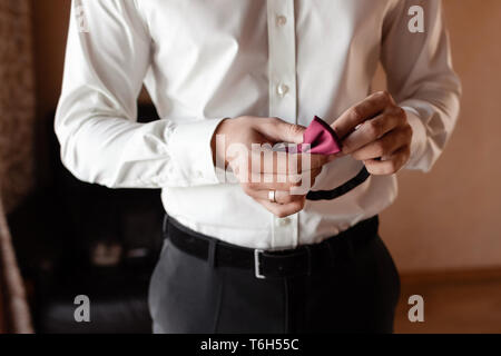 Die bräutigame morgen Vorbereitung, gutaussehenden Bräutigam anziehen und die Vorbereitung für die Hochzeit, mit einem roten Schmetterling in den Händen Stockfoto