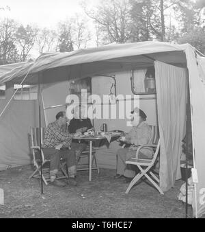 1950 s Camping. Drei Leute sitzen durch ihre Karawane genießen eine Tasse Kaffee. Die Verwendung von Wohnwagen der Sommerurlaub zu verbringen war recht zu diesem Zeitpunkt neu. Foto Kristoffersson ref BP 31-5. Schweden 1954 Stockfoto