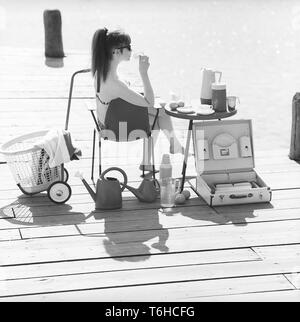 1960er jahre lifestyle. Eine junge Frau sitzt in der Sonne einen Bikini tragen. Im Bild gibt es viele der rechtzeitigen Objekte aus Kunststoff, die zu der Zeit populär waren. Vor allem, wenn Sie auf einem Sommerurlaub oder Camping. Eine Reihe von Tassen und Untertassen auf dem Tisch. Ein praktischer Fall sie in zu transportieren. Schweden der 60er Jahre Foto Kristoffersson ref DB 85-2 Stockfoto