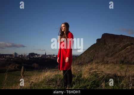 Junge Frau in langen roten Jacke steht in einem Park in Edinburgh. Stockfoto