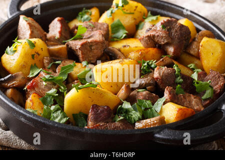 Das hauptgericht von gebratenes Schweinefleisch mit Kartoffeln und Pilzen close-up in der Pfanne auf den Tisch. Horizontale Stockfoto