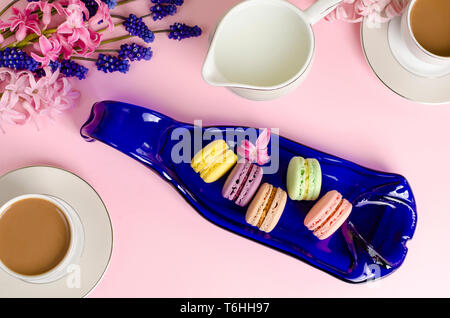 Tasse Kaffee mit Milch, Macarons, Milch Glas auf Pastell rosa Hintergrund mit muscari und Hyazinthen Blumen dekoriert. Ansicht von oben, flach. Romantische mornin Stockfoto