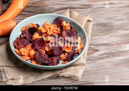 Türkis Platte mit Chips von Karotten und rote Beete auf beige Stoff auf Holztisch. Stockfoto