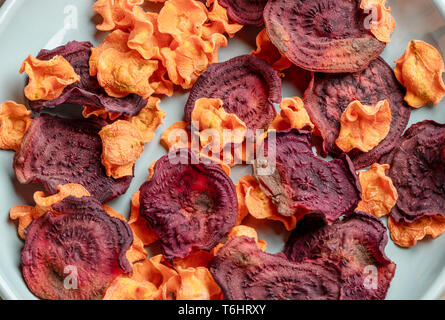 Close-up orange und rote Chips von Karotten und rote Beete auf Türkis Platte. Stockfoto