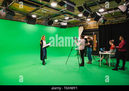 Ein Weitwinkel- aufnahme eines multi-ethnischen Gruppe von Personen, die in einem Film Studio, eine ausgereifte kaukasische Frau gesehen werden kann, die vor einem grünen scre Stockfoto