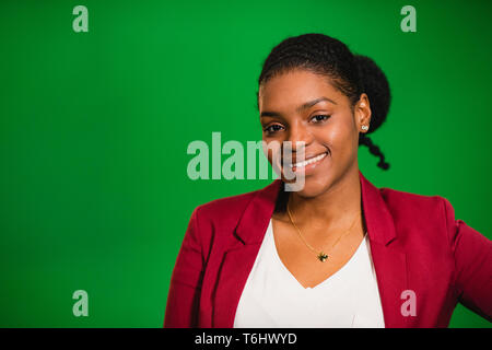Eine Frontansicht Portraitfotos eines jungen africian stehende Frau vor einem Green Screen, sie lächelt und schaut in die Kamera. Stockfoto