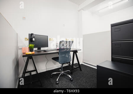 Ein Schuss von einem hölzernen Schreibtisch im Büro, am Schreibtisch, ist ein Computer, Übertopf, Papierkram und eine Auswahl an gesunden Früchten. Es gibt keine Menschen. Stockfoto