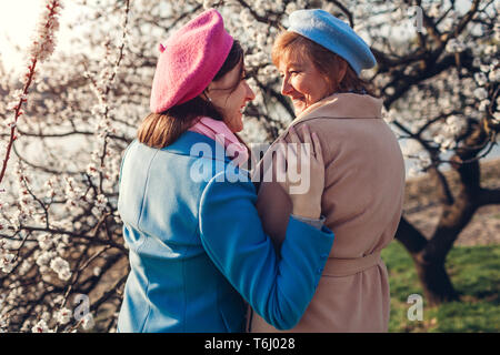 Gerne ältere Mutter und ihrer Tochter umarmen in blühende Frühling Garten bei Sonnenuntergang. Muttertag Konzept. Die Werte der Familie Stockfoto