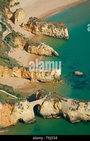 LUFTAUFNAHME. Eine Reihe paralleler Klippen am Strand von Praia Dos Estudantes (Studentenstrand), römische Brücke im Vordergrund. Lagos, Algarve, Portugal. Stockfoto