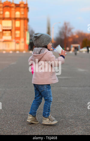 Kleine weiße Mädchen getränke Milchshake auf der Straße in den Abend. Porträt auf dem Hintergrund der Sonnenuntergang Stadtbild Stockfoto