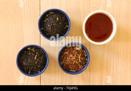 Verschiedene Sorten Tee Blätter in runde Schalen und einer Tasse Tee auf Holz- Hintergrund. Moderne minimalistische Bild in enger mit der Ansicht von oben. Stockfoto