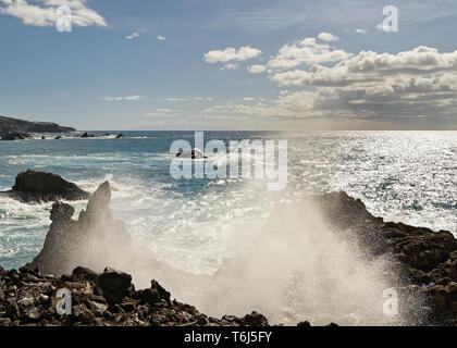 Starke Brandung auf einem schwarzen vulkanischen Strand mit Steinen, Spray Tropfen eine Welle im Gegenlicht, sun Reflexion auf dem Wasser - Ort: Spanien, Kanarische Isla Stockfoto
