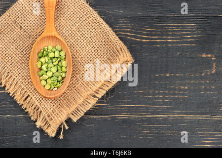 Trocken grüne Erbsen im Löffel auf Leinwand und Holz- Hintergrund, Ansicht von oben closeup Stockfoto