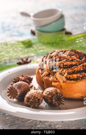 Vertikale Foto von mehreren Braun poppy Köpfe auf weiße Platte. Poppy Köpfe sind neben süßen Brötchen mit Mutter Schichten platziert. Einige Stücke von Anis Sterne sind auf Stockfoto