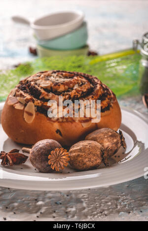 Vertikale Foto von mehreren Braun poppy Köpfe auf weiße Platte. Poppy Köpfe sind neben süßen Brötchen mit Mutter Schichten platziert. Einige Stücke von Anis Sterne sind auf Stockfoto