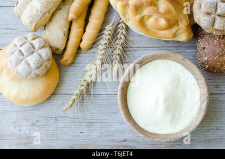 Verschiedene Arten von traditionellen Italienischen frisch gebackenes Brot und Brötchen mit Schüssel Mehl auf hölzernen Tisch Hintergrund. Rustikale Vintage Style. Ansicht von oben. Stockfoto