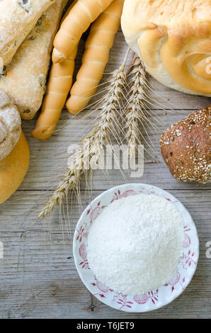 Verschiedene Arten von traditionellen Italienischen frisch gebackenes Brot und Brötchen mit Schüssel Mehl auf hölzernen Tisch Hintergrund. Rustikale Vintage Style. Ansicht von oben. Stockfoto
