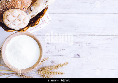 Verschiedene Arten von traditionellen Italienischen frisch gebackenes Brot und Brötchen mit Schüssel Mehl auf hölzernen Tisch Hintergrund. Rustikale Vintage Style. Ansicht von oben. Co Stockfoto