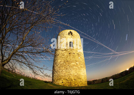 Alten Wachturm in der Nacht vom Vollmond beleuchtet, mit rotierenden Sky (Star Wanderwege) und ebene Wanderwege (Foto mit Fish Eye Objektiv aufgenommen) Stockfoto