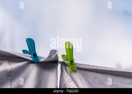 Weiße Kleidung hingen auf einer Wäscheleine zum Trocknen und durch die Kleidung befestigt Pflöcke gegen den blauen Himmel im hellen warmen sonnigen Tag Stockfoto