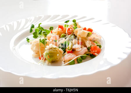 Couscous mit Gemüse, Garnelen und Radieschen auf einem weißen Teller Stockfoto