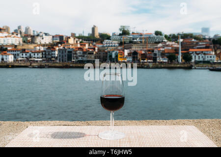 Selektiver Fokus der kleinen Glas roten Portwein mit Blick auf Vila Nova de Gaia Bahndamm bei Cais da Ribeira am Fluss Douro in Porto, Portugal Stockfoto