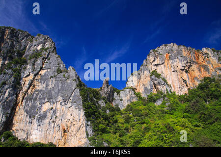 Bootsfahrt entlang der Küste der tropischen Insel Ko Phi Phi entlang beeindruckend steile rote Felswand hoch in den blauen Himmel, Andaman Sea, Thailand Stockfoto