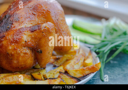 Huhn aus dem Ofen auf einem weißen Teller mit grünen und Kartoffeln mit einer goldenen Kruste Stockfoto