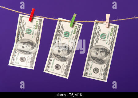 Einhundert Dollar hängen auf Wäscheleine mit Holz- Clips auf blauem Hintergrund. Stockfoto