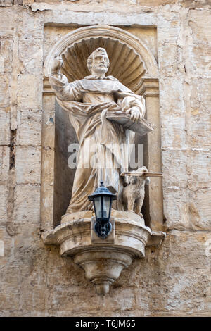 Der geschnitzte statue Statue des hl. Dominikus mit seiner Fackel, Hund, in eine Nische in der Wand im St Nicholas Street in Valletta, Malta Stockfoto