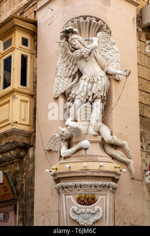 Eine Statue des Erzengels Michael trampeln auf Satan stand auf einem Sockel an der Ecke von St. Ursula und Erzbischof Straßen in Valletta. Stockfoto