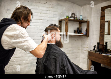Brutaler Kerl in der modernen Friseur. Friseur Frisur macht ein Mann mit einem langen Bart. Master Friseur nicht Frisur mit Haarschneider Stockfoto