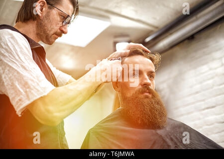 Brutaler Kerl in der modernen Friseur. Friseur Frisur macht ein Mann mit einem langen Bart. Master Friseur die Frisur von Schere und Kamm Stockfoto