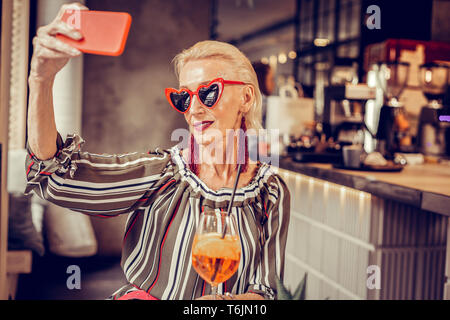 Modische ältere Frau in Herzform Sonnenbrille tragende rote Smartphone Stockfoto