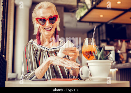 Schöne alte Frau in funky Sonnenbrillen Anwendung Pflegecreme Stockfoto