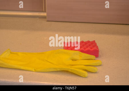 Reinigung der Arbeitsgeräte in der Küche Gummihandschuhe und Schwamm liegen auf die verschmutzte Oberfläche des Tisches, das Konzept der Sauberkeit Kopie Raum, la Licht aus Led Stockfoto