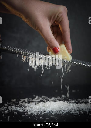 Hand einer Frau Gitter Parmesan auf schwarzem Hintergrund. Dunkle essen. Italienische Käse Parmigiano Reggiano Stockfoto