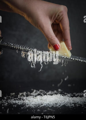Hand einer Frau Gitter Parmesan auf schwarzem Hintergrund. Dunkle essen. Italienische Käse Parmigiano Reggiano Stockfoto
