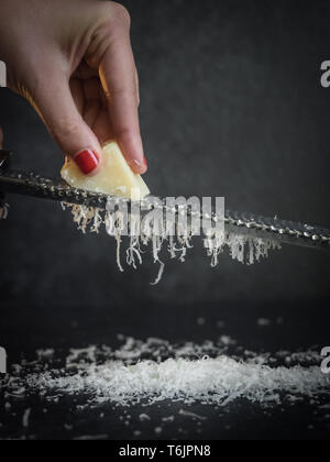 Hand einer Frau Gitter Parmesan auf schwarzem Hintergrund. Dunkle essen. Italienische Käse Parmigiano Reggiano Stockfoto