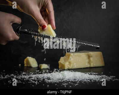 Hand einer Frau Gitter Parmesan auf schwarzem Hintergrund. Dunkle essen. Italienische Käse Parmigiano Reggiano Stockfoto